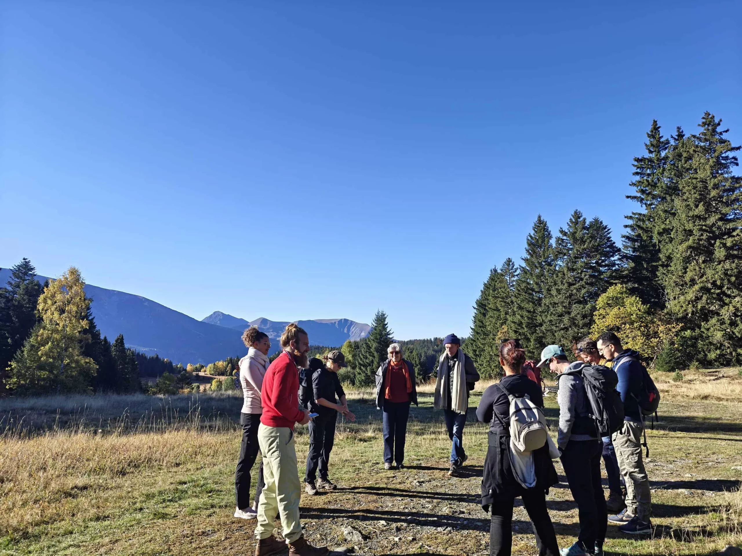 Groupe de personnes en randonnée dans un paysage naturel avec montagnes et arbres.