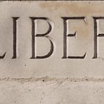 Sculpture représentant le mot "Liberté" en relief sur un mur en pierre.