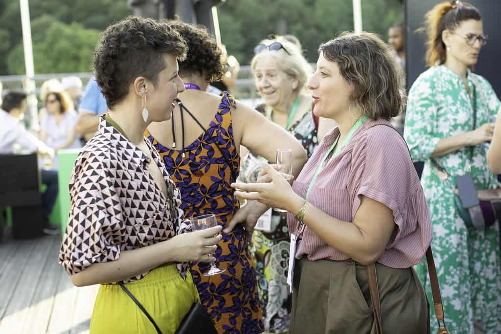 Deux femmes discutent lors d'un événement en plein air, échangeant dans une ambiance conviviale et p.